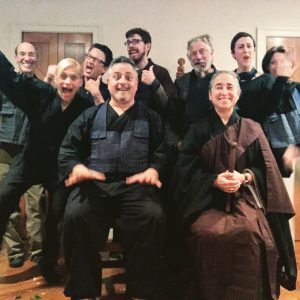 9 people wearing robes and/or rakusus with joyful expressions